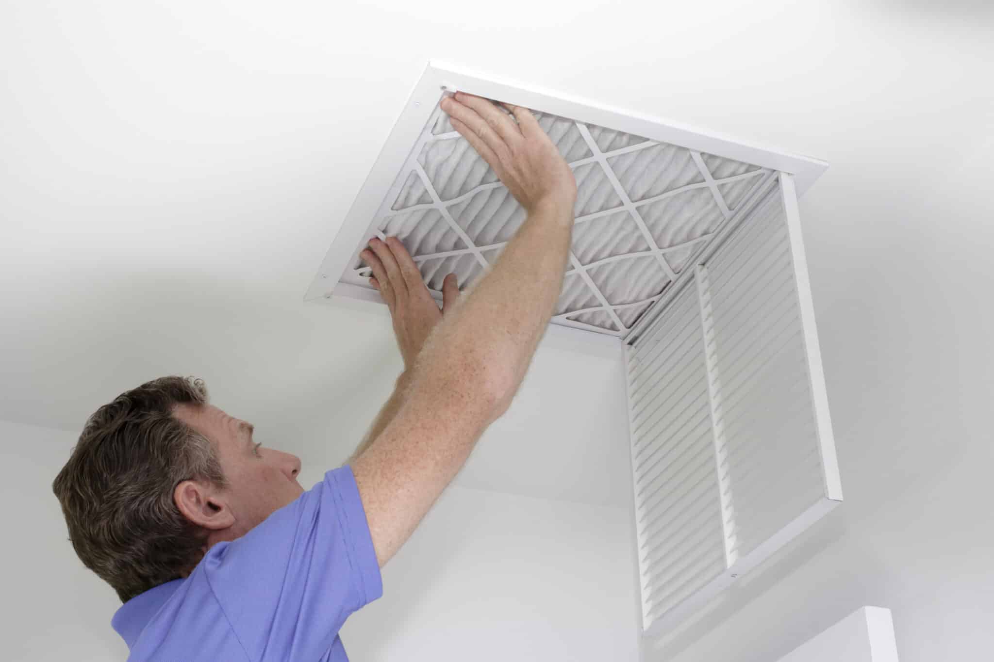 A man is pushing a clean HVAC filter into place in the ceiling with both hands. HVAC Filter by One Hour Heating & Air Conditioning of San Diego