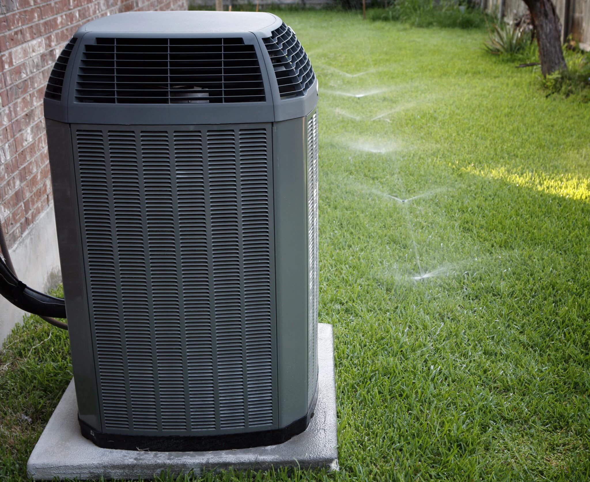 Modern high-efficiency HVAC system in the backyard with a working sprinkler system.