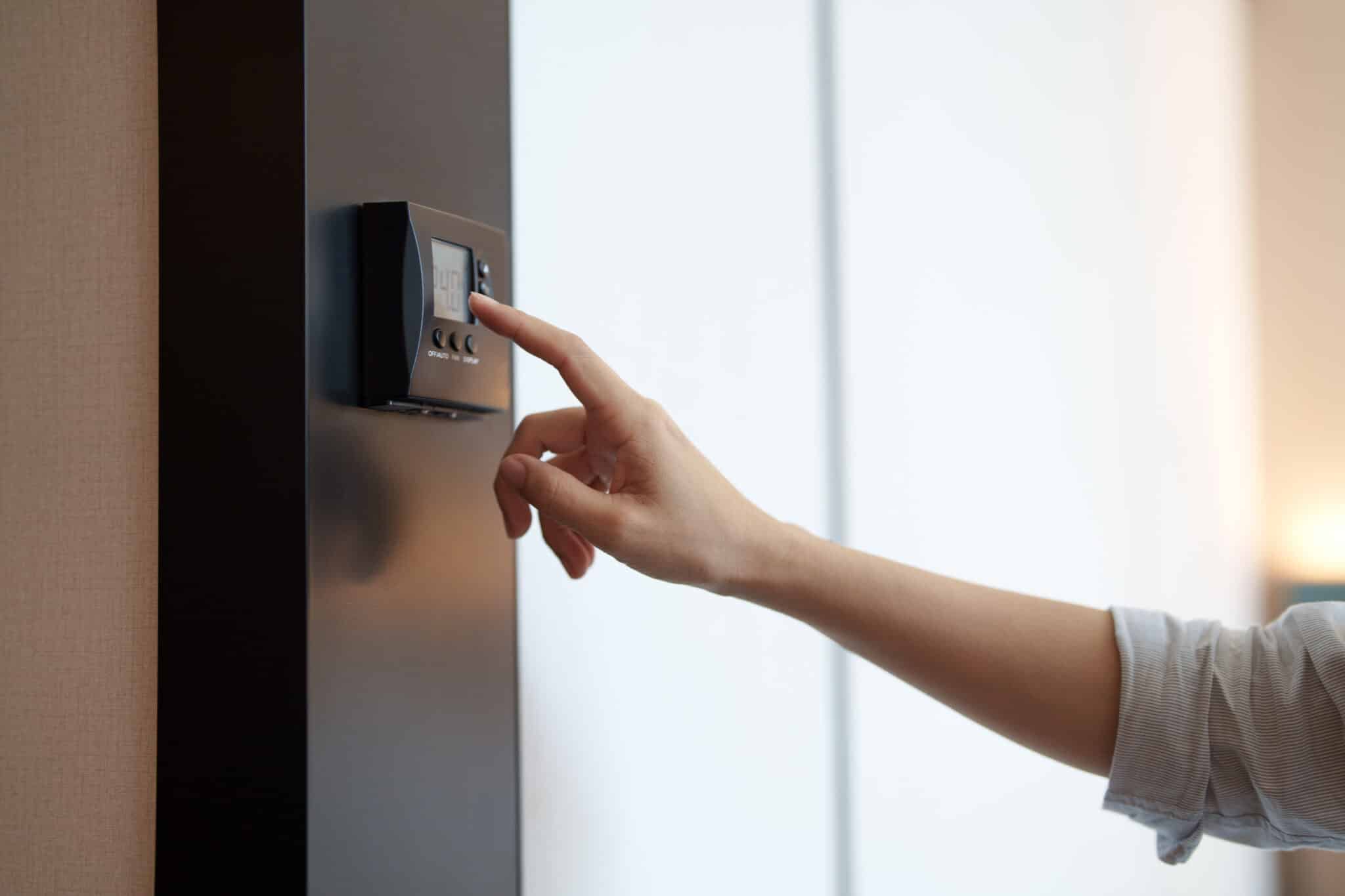 Using a smart thermostat, a woman adjusts the HVAC system temperature at home.