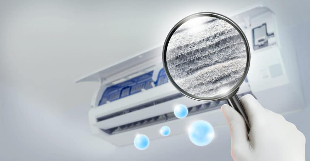 Common indoor air pollutants include dust and dirt inside an air conditioner filter, seen through a magnifying glass.