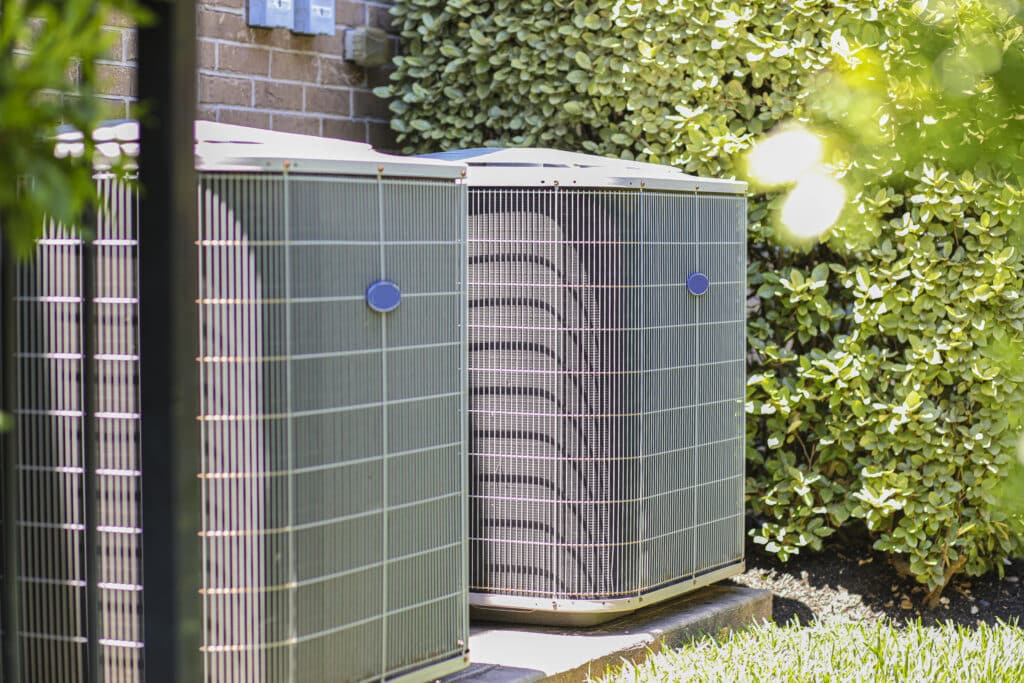 An air conditioning unit is installed outdoors in the side yard of a brick home during the hot summer season, naturally cooling the interior.